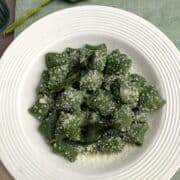 Gnocchi di ricotta e spinaci su un piatto bianco e lino verde. Gli gnocchi sono conditi con parmigiano grattugiato
