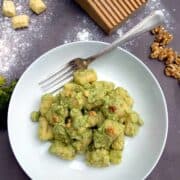 Gnocchi al Pesto di Broccoli in un piatto bianco con forchetta su tavolo di legno scuro. I gnocchi sono serviti con gherigli di noci.