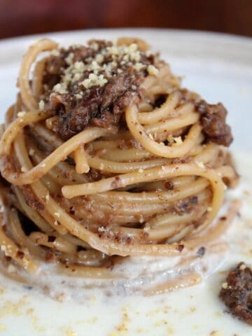 Spaghetti con radicchio Tardivo in un piatto bianco. La pasta poggia su uno strato di formaggio ed è condita con radicchio e gherigli di noci