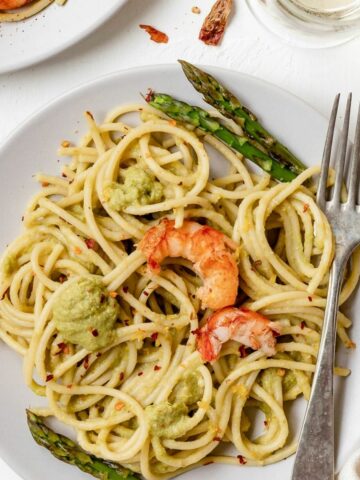Una vista dall'alto Spaghetti agli asparagi con gamberi in un piatto bianco con una forchetta. Viene guarnito con asparagi e gamberoni.