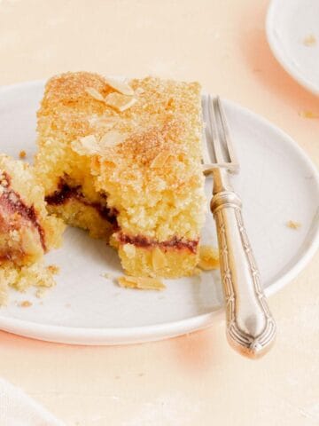 Primo piano di una fetta di Crostata Sabbiata con marmellata su un piatto bianco con una forchetta. La fetta mostra la marmellata all'interno della torta
